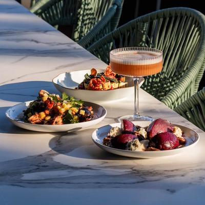 Outdoor marble table set with small sharing plates of food and a cocktail.