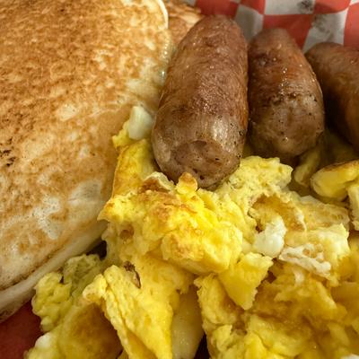 Close up of a breakfast plate with pancakes, scrambled eggs, and sausage links.