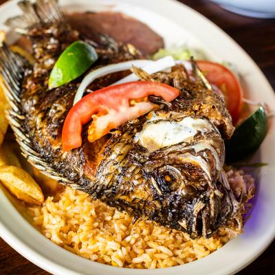 Whole fried fish served over rice with beans, tomato, lime, and onions.