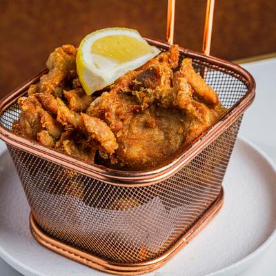 Chicken Karaage served in a  metal frying basket with a lemon wedge.
