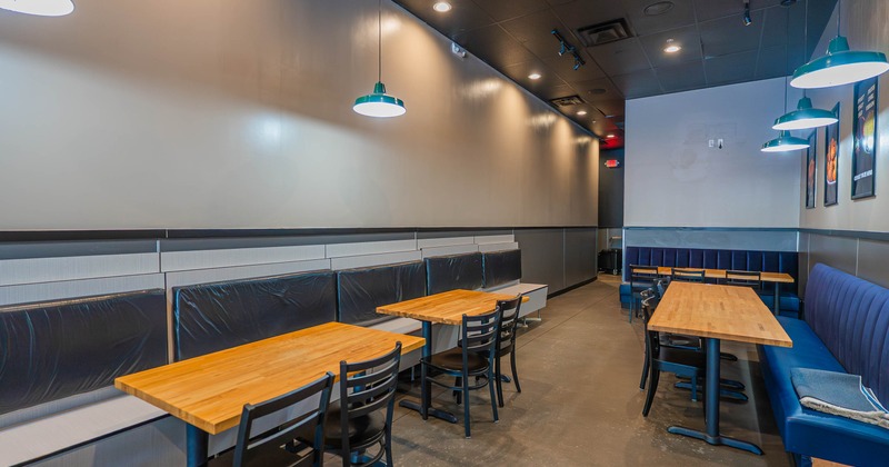 Interior of a modern restaurant with wooden tables, black chairs, and teal pendant lights