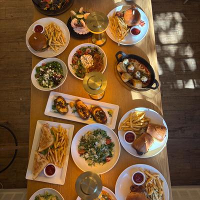 Assorted burgers, salads, and appetizers on a wooden table with golden lamps.