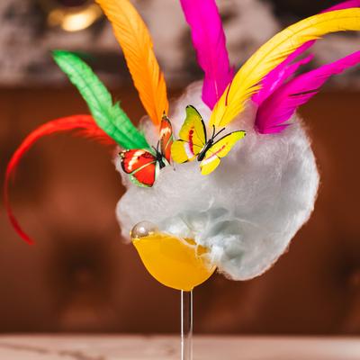 A colorful cocktail adorned with multi colored feathers, butterflies and fluffy clouds.
