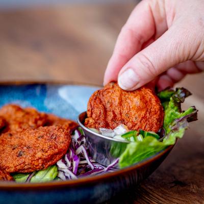 Hand dipping a Thai fish cake into sauce.