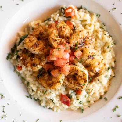 Risotto topped with grilled shrimp and diced tomato, overhead view.