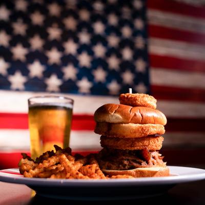 Bacon Jam Burger and fries served with beer, with the US flag in the background.