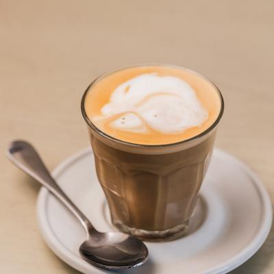 Latte in a clear glass on a white saucer.