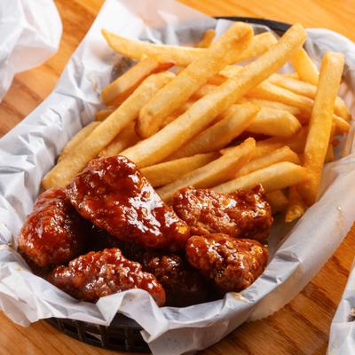 Boneless wings coated in sauce and served in basket with a side of fries.