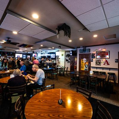 Interior with multiple round tables and chairs, a bar area and several televisions.