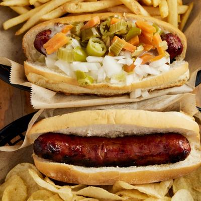 Two hot dogs, one of which is topped with peppers and onions, and the other is a plain hot dog.