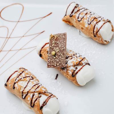 Cannoli topped with powdered sugar and chocolate drizzle.