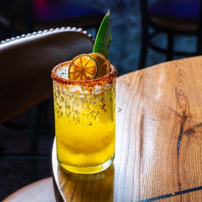 Cocktail in rimed glass, garnished with dried citrus slices and pineapple leaf.