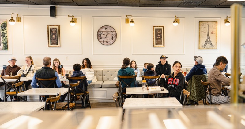 People dining in a busy cafe with Paris-themed art
