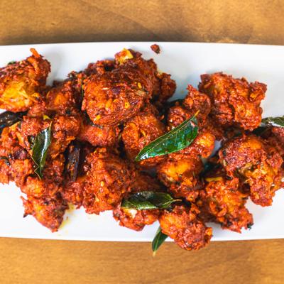 Spicy Indian fried chicken with red masala coating and curry leaf garnish.