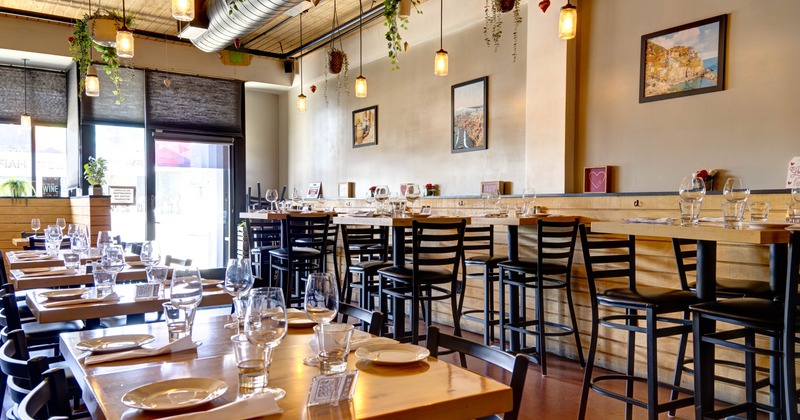 Interior with wooden tables set for dining, black chairs, hanging lights, and framed pictures on the wall
