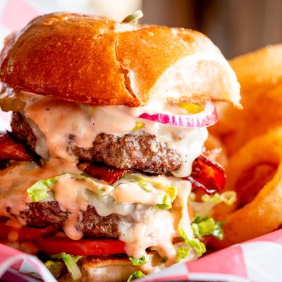 Double cheeseburger with sauce, lettuce, onions, and bacon on a brioche bun.