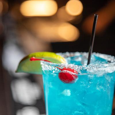 Close up of a glass of Blue margarita garnished with a cherry and a lemon slice.