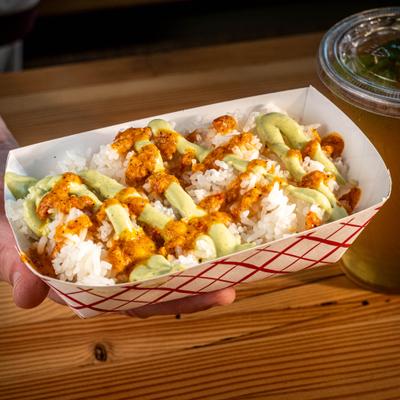 Hand holding a cardboard box with white rice drizzled with sauces.