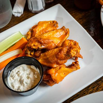 Buffalo chicken wings served with carrot and celery sticks, and a creamy dipping sauce.