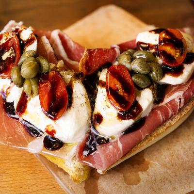 Prosciutto Bruschetta topped with stracciatella, capers, cherry tomatoes and balsamic glaze.