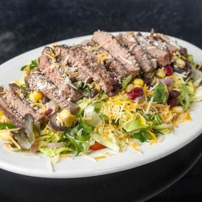Steak salad with lettuce, corn, beans, and shredded cheese.