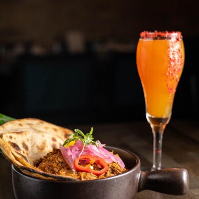 Shredded Lamb bites pot and a glass of an orange cocktail drink