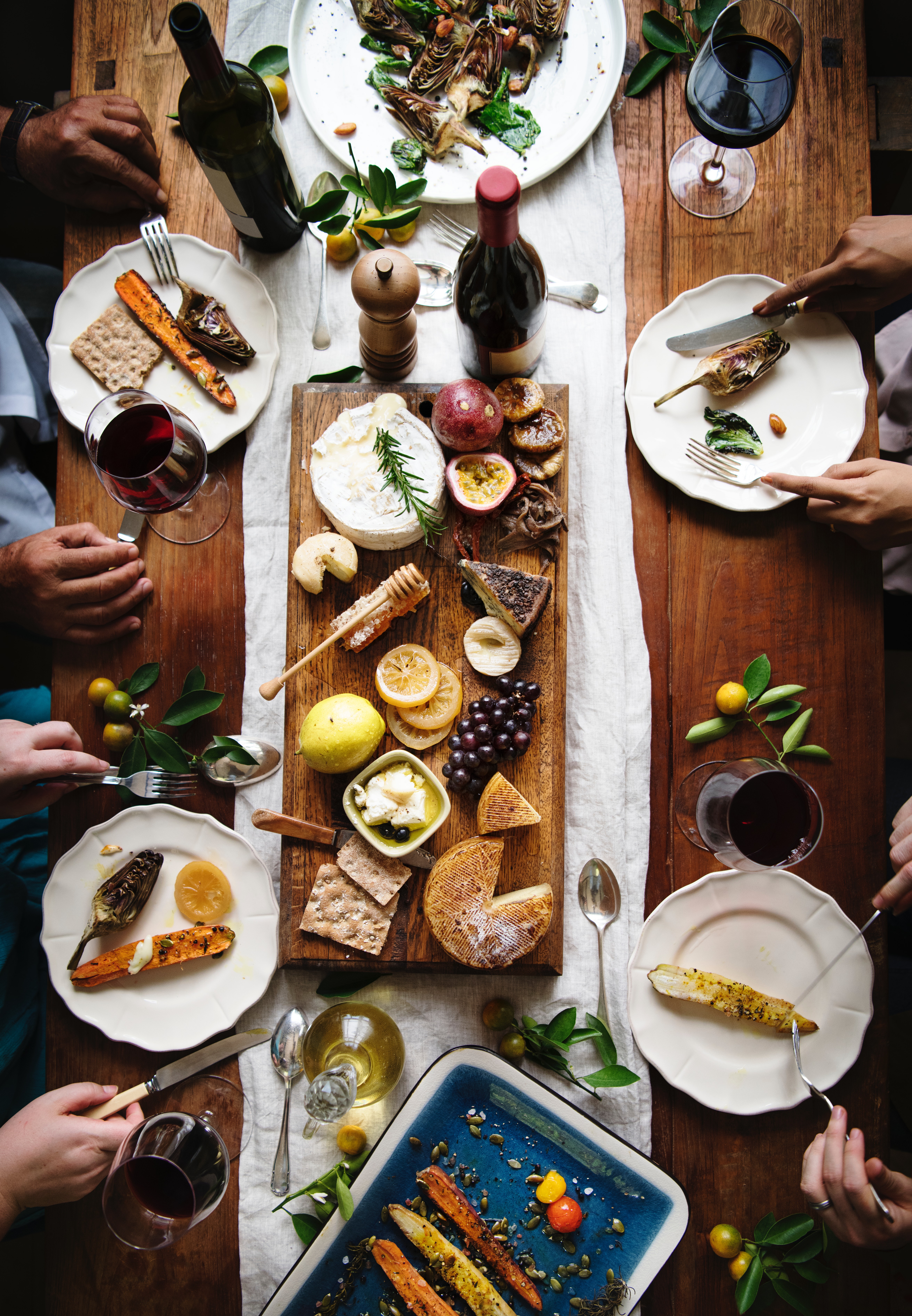 A group of guests enjoying food from a cheese platter and wine at table, top view