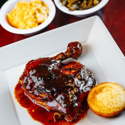 Chicken leg with BBQ sauce, cornbread, and side dishes.