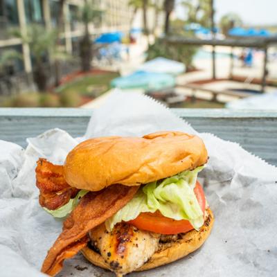 Grilled chicken sandwich with bacon, lettuce, and tomato served on parchment paper outdoors.