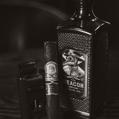 A cigar and a cutter sit next to a bottle of scotch whiskey.