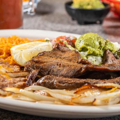 Carne Asada served with grilled onions, beans, rice, guacamole and a lemon wedge.