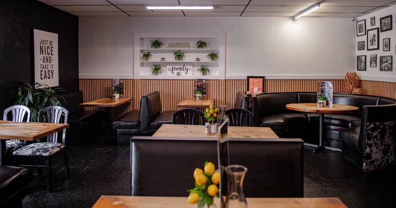 Cozy café interior with wooden tables, black leather benches, plants and framed pictures as decor