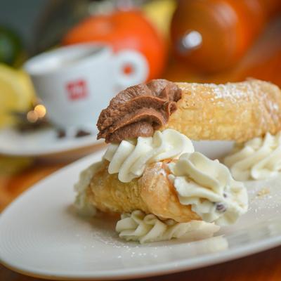 Two cannolis, one filled with chocolate cream, the other with sweet ricotta.