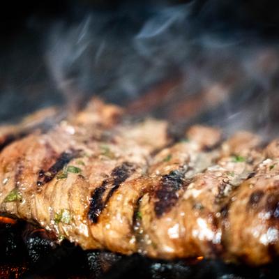 Grilled meat cooking over open flames with smoke rising.