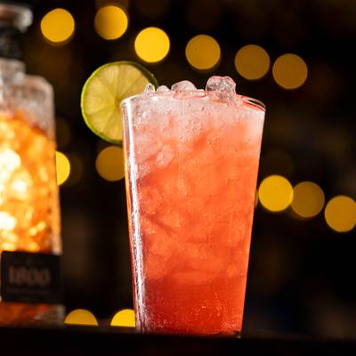 Pink cocktail in a tall glass with crushed ice and lime wheel garnish.