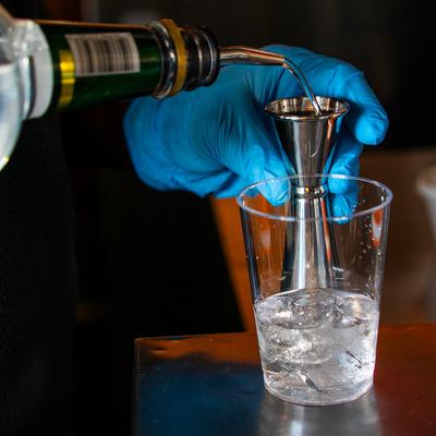 A bartender pouring a drink into a glass using a jigger.