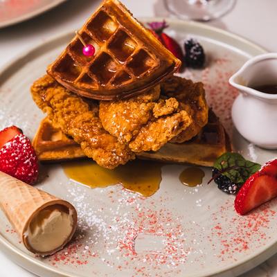 A plate of chicken and waffles  with berries, an ice cream cone, and syrup.