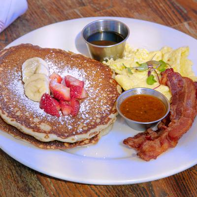 Pancakes, with bananas, strawberries, scrambled eggs, bacon, and maple syrup.