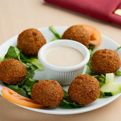 Falafel balls served on a bed of lettuce surrounding a cup of creamy sauce.