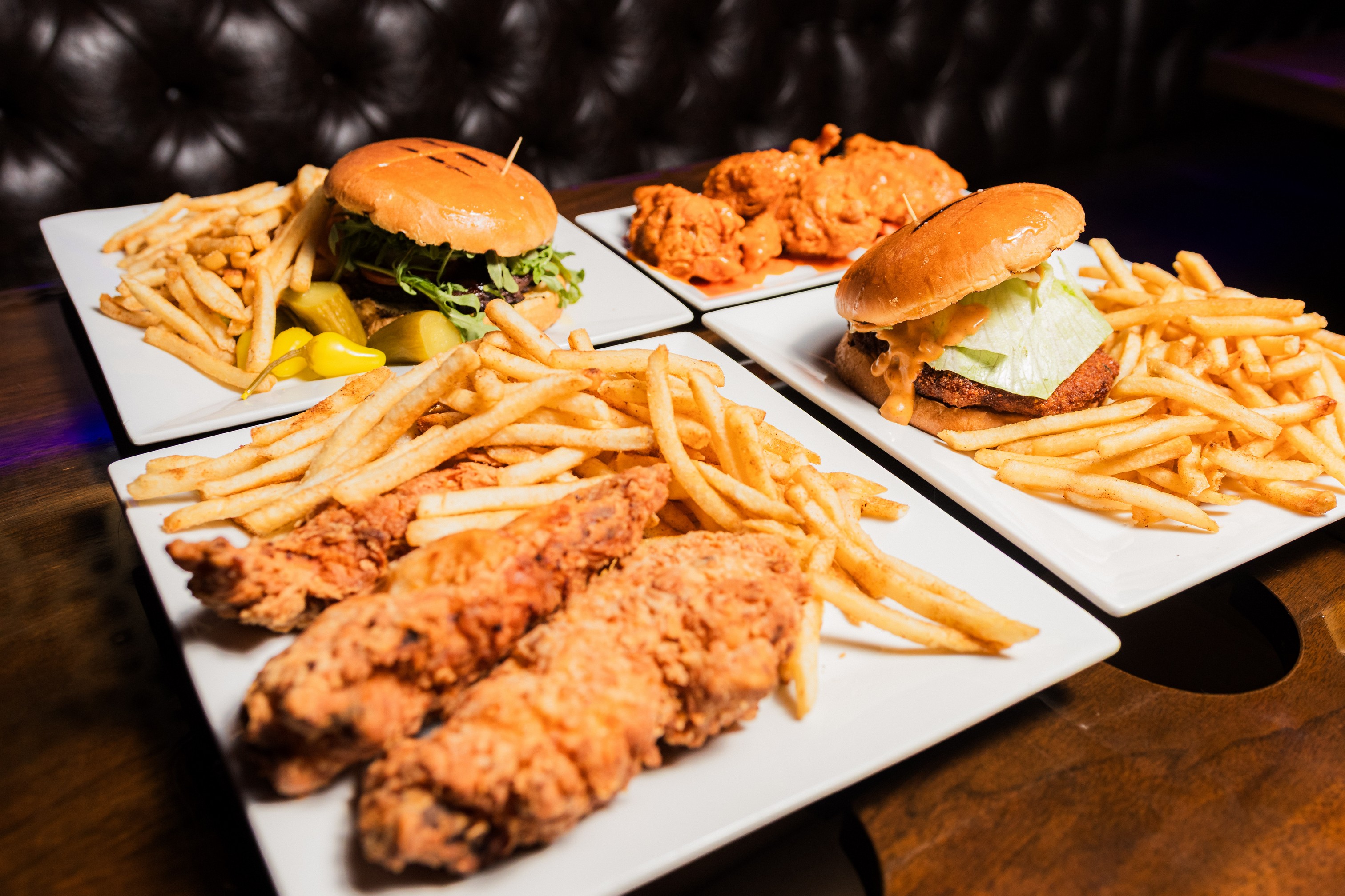 Couple of burgers served on the table with plate of tenders and wings