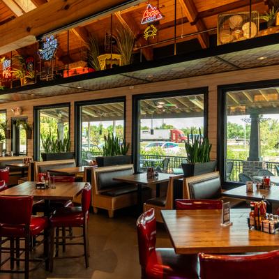 Bright dining room with booths, wooden tables, large windows, and neon signs.
