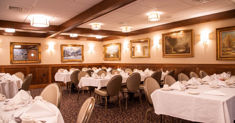 Interior, tables with white table cloths, cutlery and tableware, pictures on walls