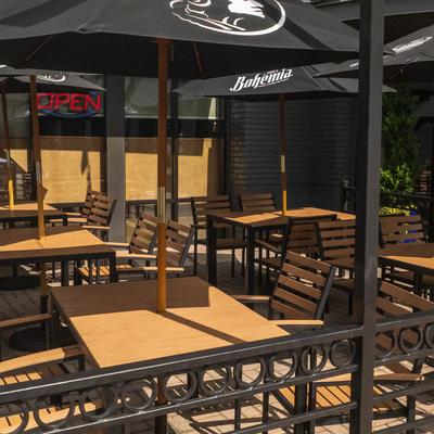 Outdoor restaurant patio with wooden tables, black umbrellas, and metal railings.