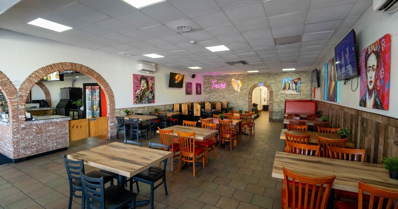Colorful interior with wooden tables, vibrant paintings and a neon "Tacos" sign