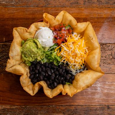 Taco Salad featuring beans, cheese, sour cream, and guacamole inside a crispy tortilla shell.