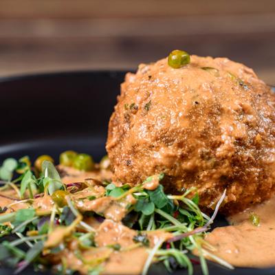 Arancini topped with creamy sauce, garnished with microgreens and peas.