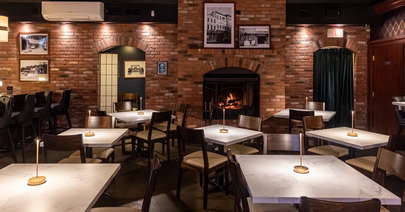 Cozy interior - brick walls, lit fireplace, stone tables, wooden chairs and photos on the wall