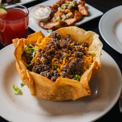 Taco salad in a tortilla bowl with seasoned beef and cheese, paired with a cocktail.