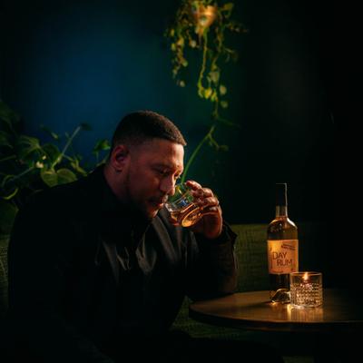 A person sipping a drink at a candle-lit table with a rum bottle.