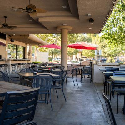 Outdoor patio seating area with tables, chairs, bar, and red umbrellas on a sunny day.